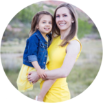 A woman in a yellow dress holds a young girl in a matching dress with a denim jacket, both smiling outdoors.