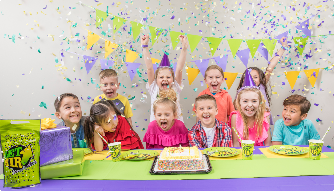 Children celebrating at a birthday party with cake, confetti, and raised hands.