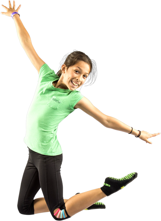 A joyful girl in a green t-shirt and black leggings jumps with arms outstretched, smiling brightly against a white background.