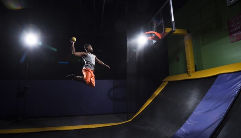 Man in orange shorts jumping high to dunk.