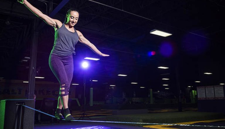 Woman balancing on a slackline with club lighting.