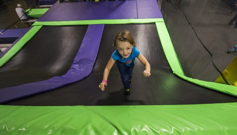 Young girl running up a trampoline slide.