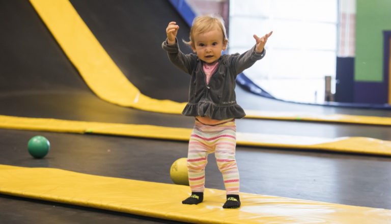 Toddler standing on trampoline with arms raised.