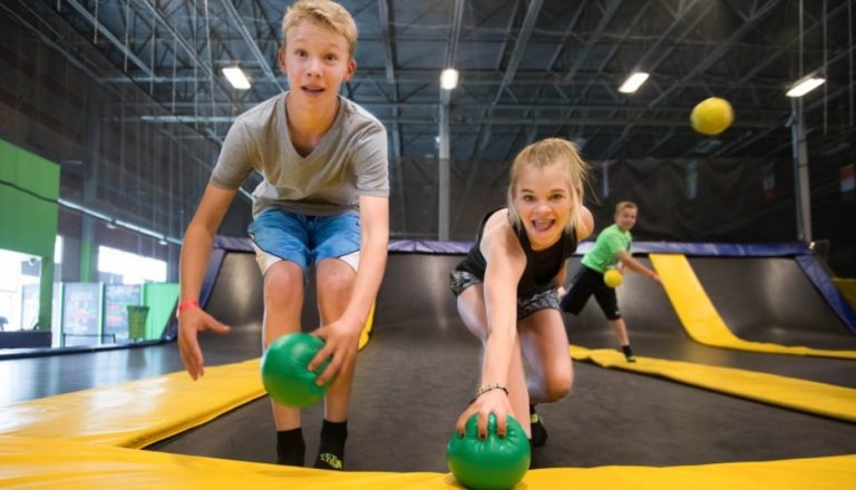 Two kids reaching for dodgeballs on trampolines.