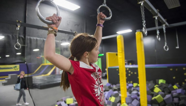 Girl swinging on rings over a foam pit.