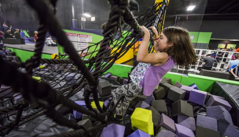 Girl climbing a rope net over a foam pit.