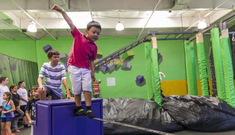 Boy balancing on a slackline with a group watching.