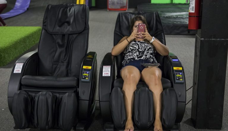 Woman relaxing in a massage chair with a phone.