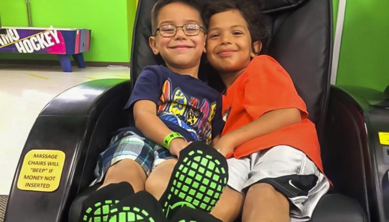 Two boys sitting on a massage chair, smiling.