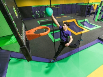 Boy playing trampoline basketball, reaching for the hoop.